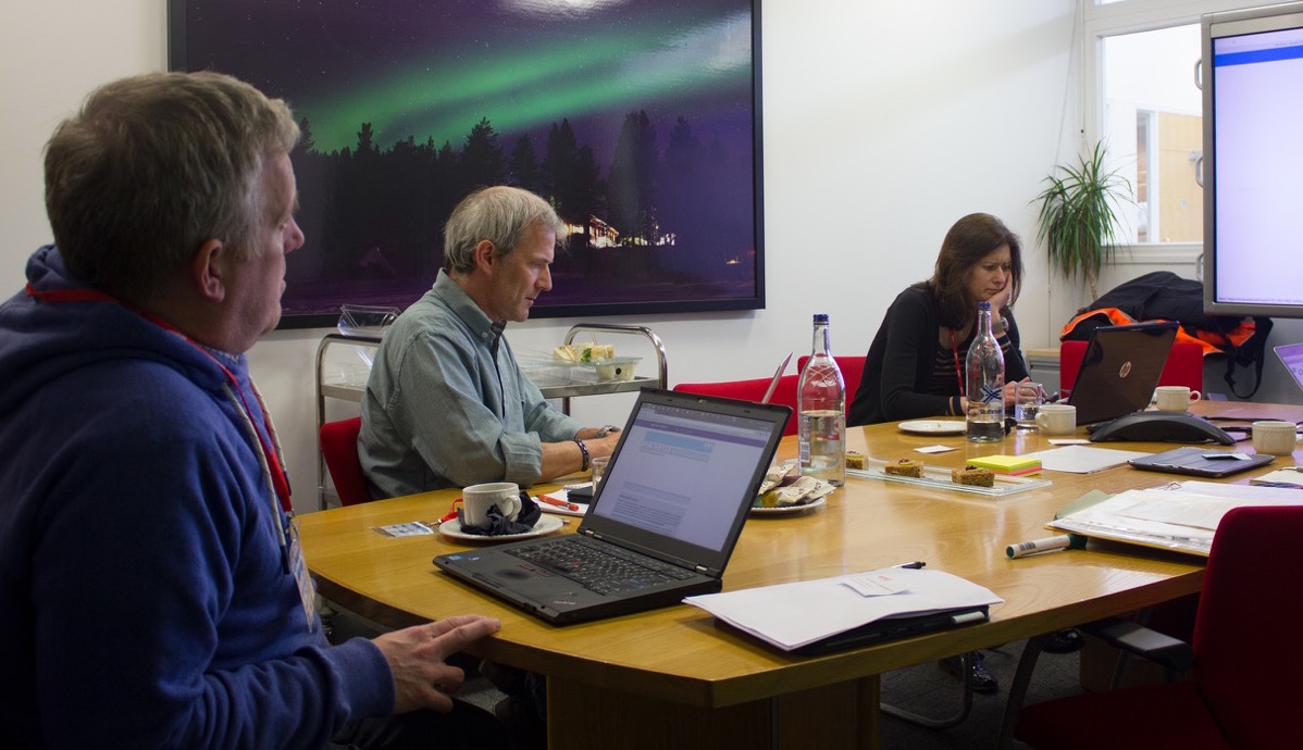 people in a boardroom watching a presentation with laptops